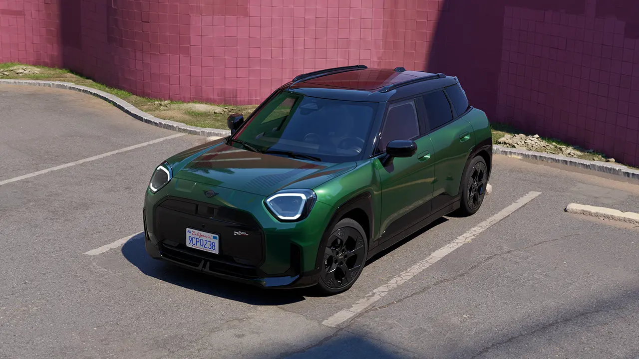 Vy framifrån av en helt elektrisk MINI Aceman i British Racing Green på en parkeringsplats med en rosa vägg i bakgrunden