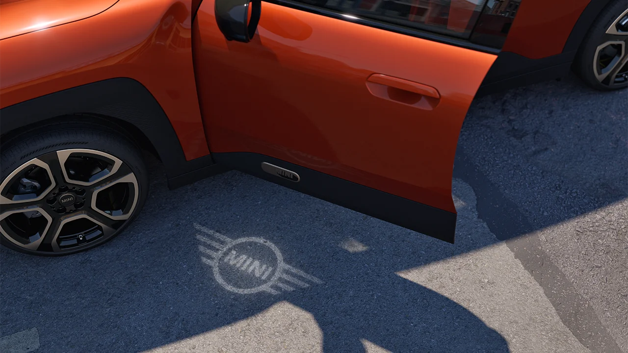 Exteriörvy över helt elektriska MINI Aceman med öppen dörr och välkomstbelysning i form av MINIs logotyp på marken