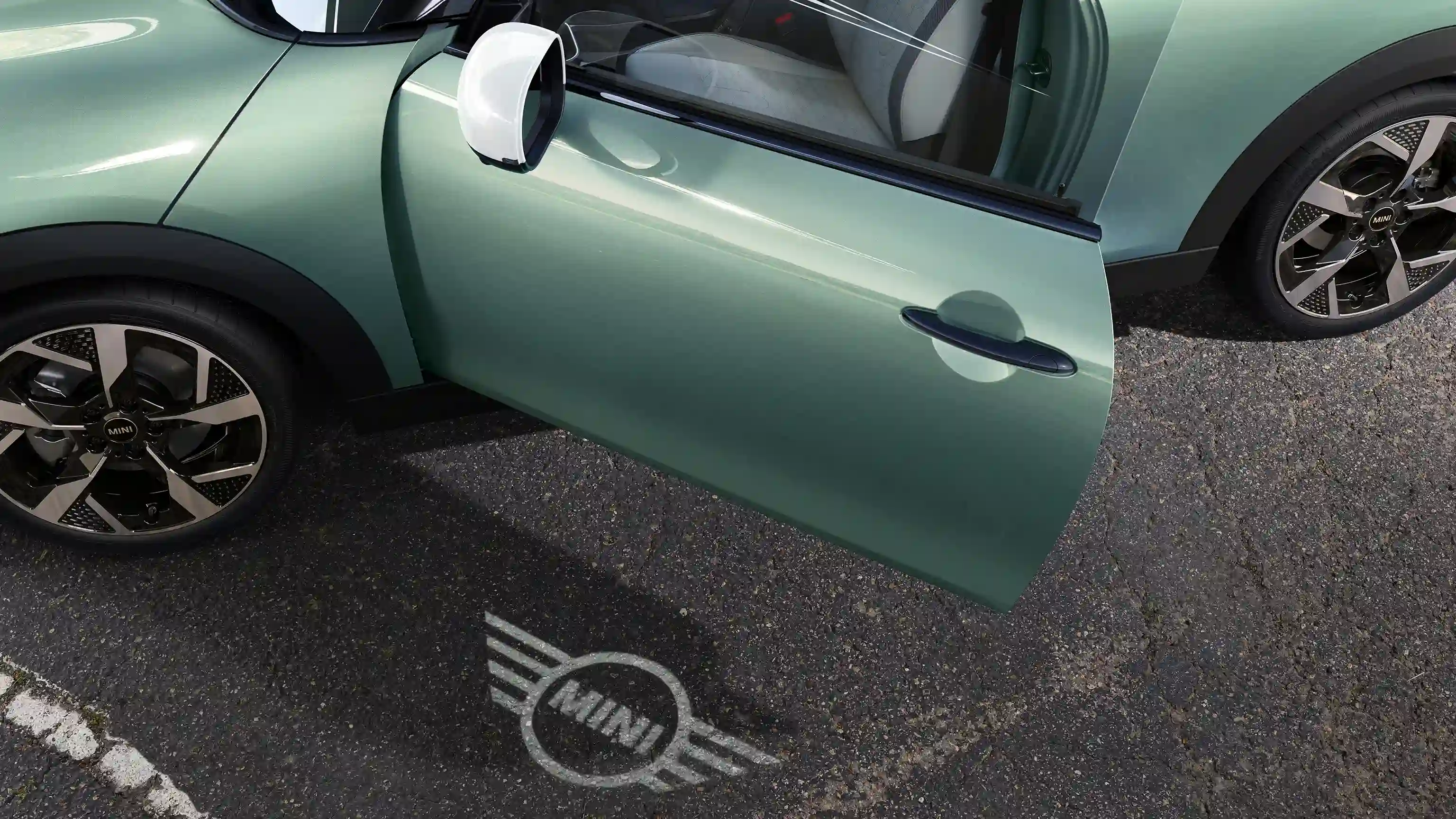 Exteriörvy av en MINI Cooper med öppen dörr och välkomstbelysning i form av MINIs logotyp på marken 