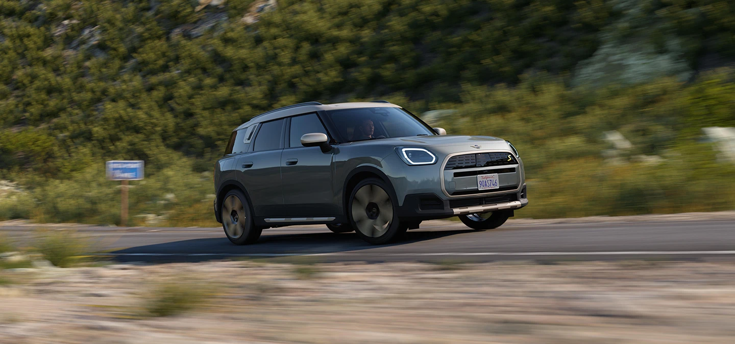 Sidovy av en helt elektrisk MINI Countryman i Smokey Green med tak i Vibrant Silver under körning.