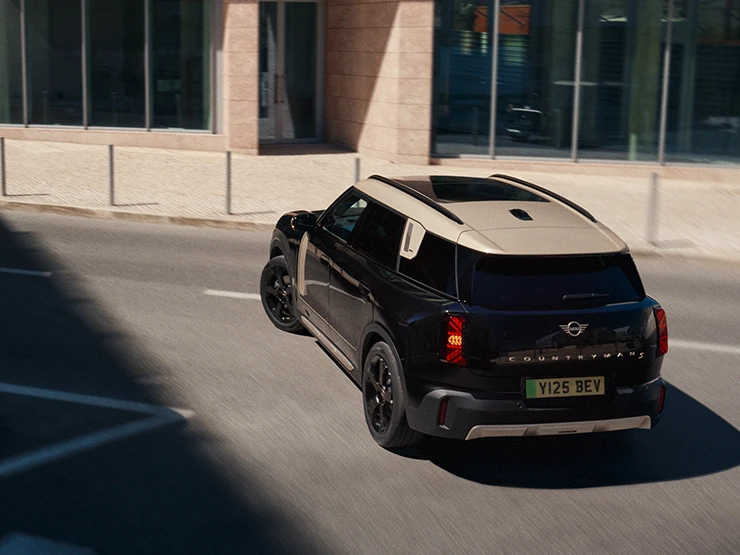 Vy bakifrån av en helt elektrisk MINI Countryman i Midnight Black med tak i Vibrant Silver som parkerar,