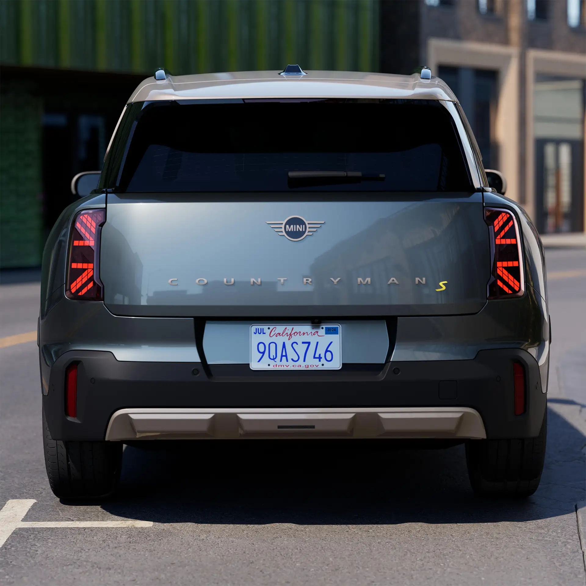 Vy bakifrån av en helt elektrisk MINI Countryman i Smokey Green med tak i Vibrant Silver som parkerar
