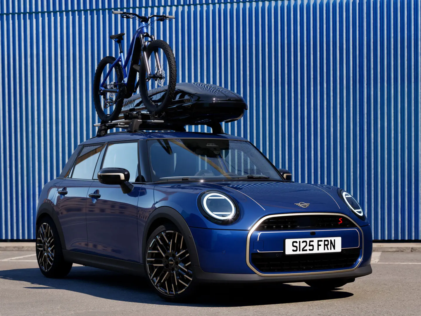 Frontvy av MINI Aceman i Indigo Sunset Blue med MINI takcykelhållare, med en mountainbike, och MINI takbox 320.