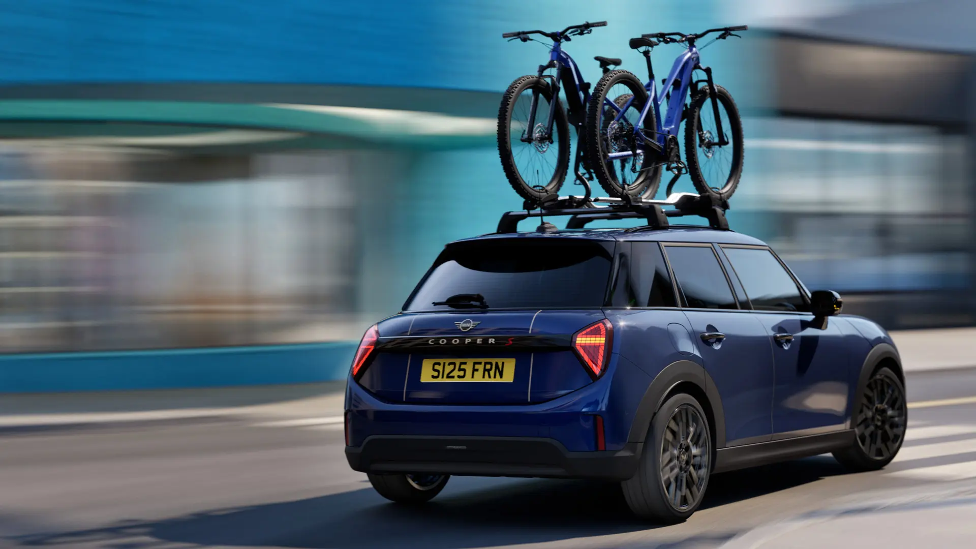 MINI Aceman i Indigo Sunset Blue utrustad med MINI takcykelhållare, med två mountainbikes, vy snett bakifrån. 