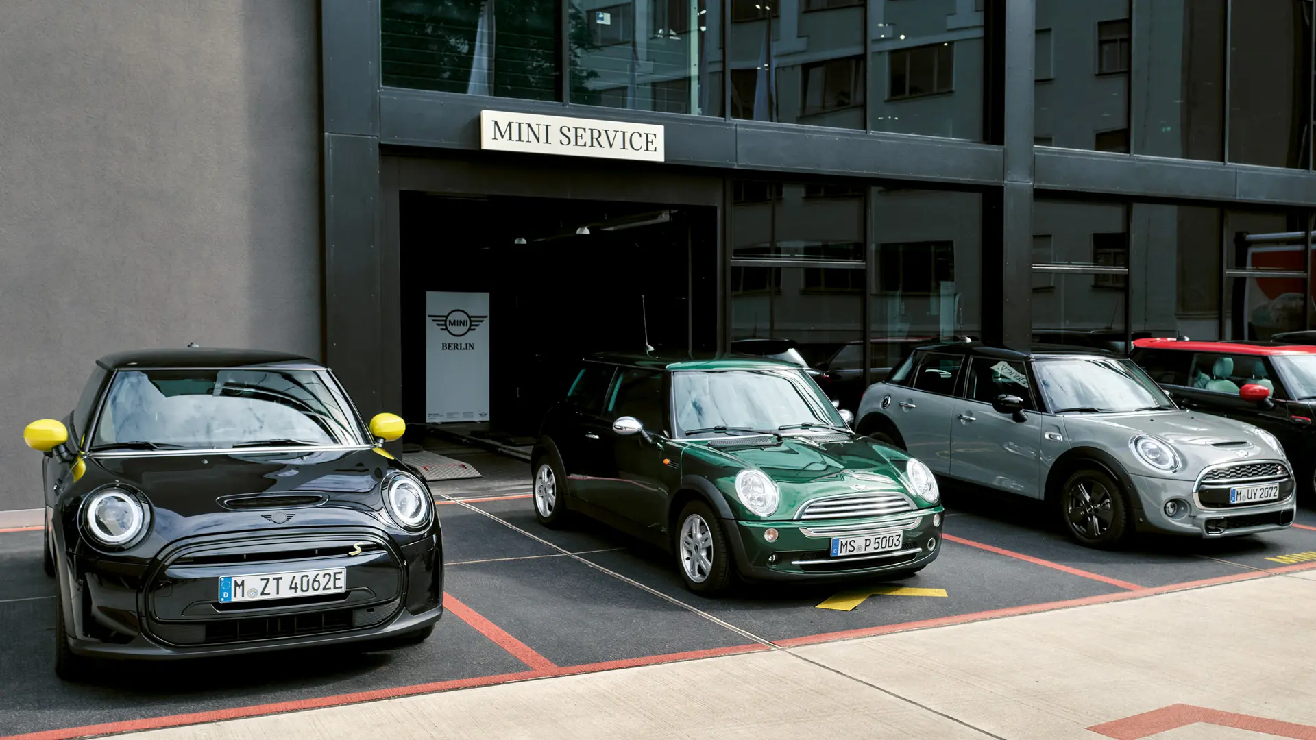 MINI Cooper Electric S i svart står utanför ett MINI center bredvid en MINI Cooper 3-dörrars i grönt, MINI 5-dörrars i silver, MINI JCW svart, sedda framifrån. 